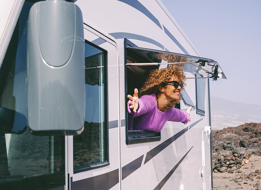 Contact - View of a Cheerful Middle Aged Woman Wearing Sunglasses Sticking her Head and Hands Out the Window During an RV Trip Along the Coast