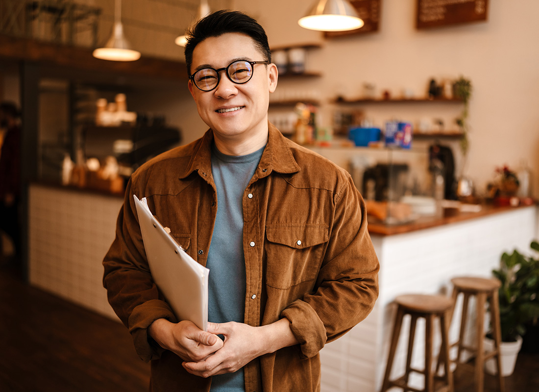 Insurance by Industry - Portrait of a Middle Aged Small Business Owner Holding Papers Under his Arm Standing in a Small Empty Cafe