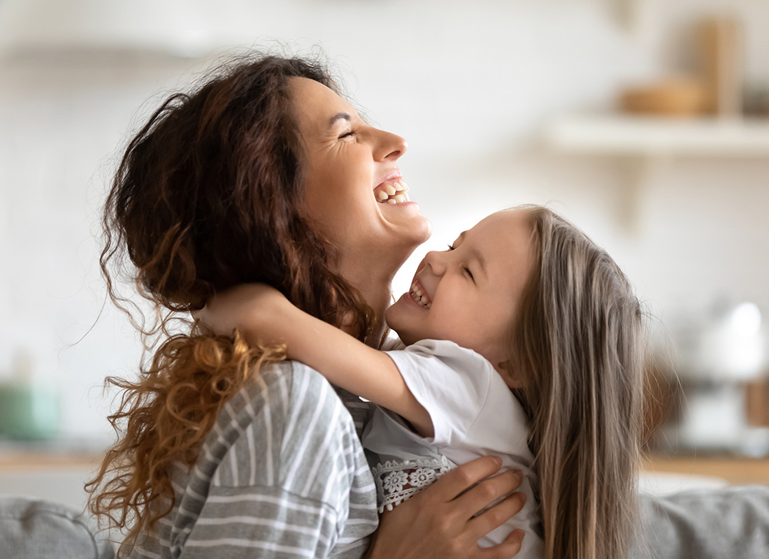 Life Insurance - Closeup Portrait of an Excited Daughter Having Fun Hugging and Playing with her Mother at Home